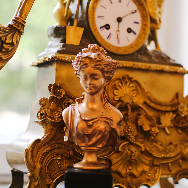 Kvinnlig guldfärgad byst framför guldklocka